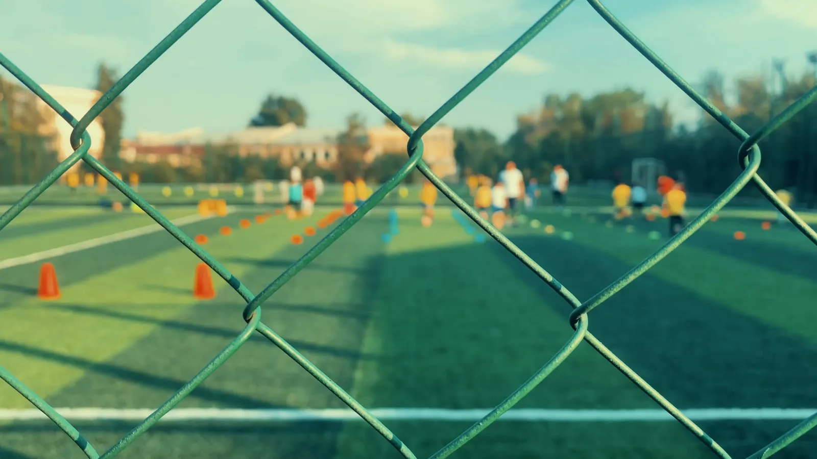 Training pitch seen through a chain-link fence with cones laid out