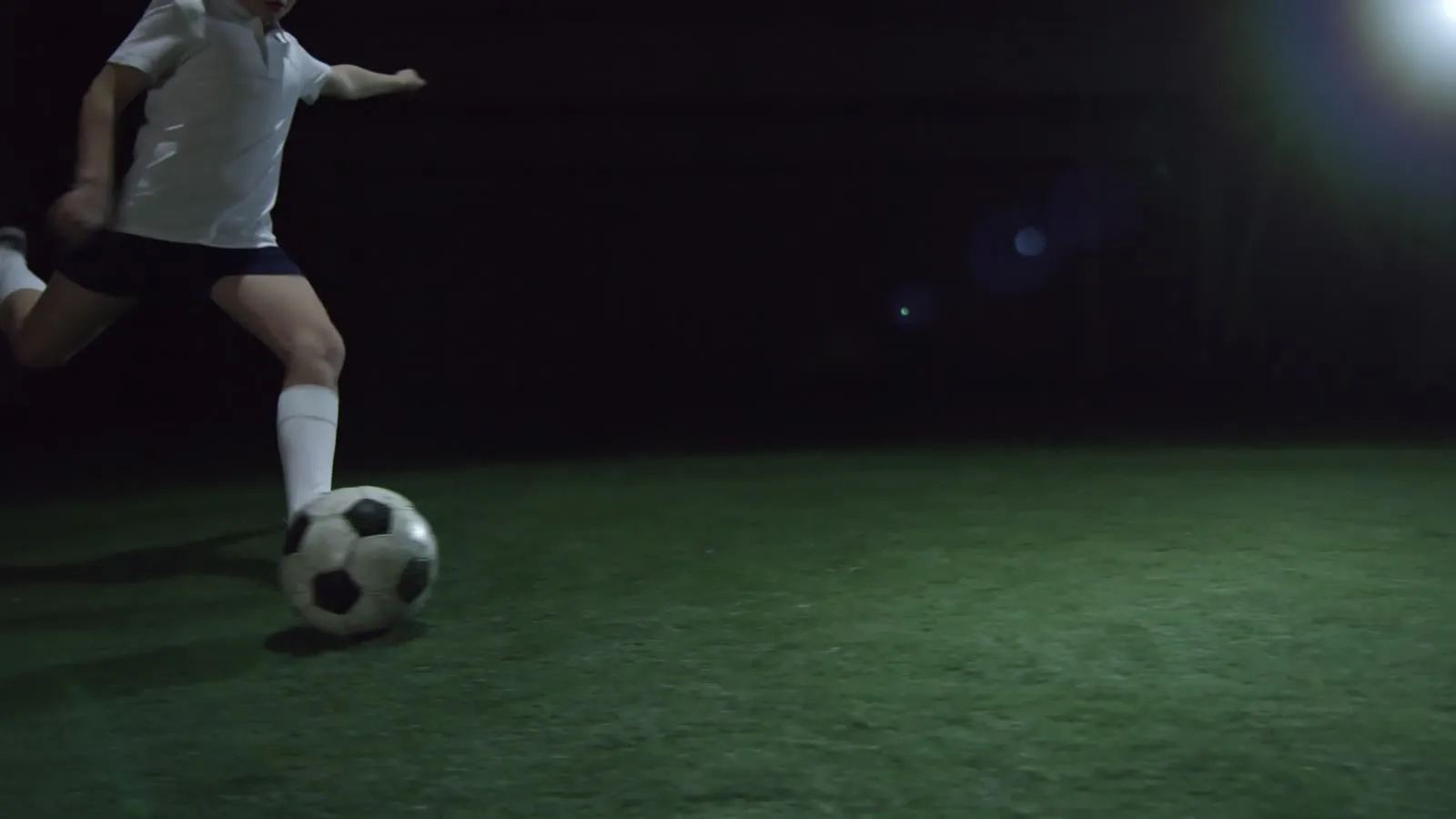 Player striking a ball under floodlights at night
